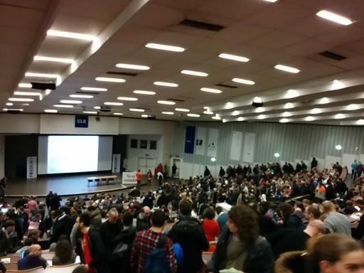 Primera charla de la FOSDEM con gente sentada en el pasillo